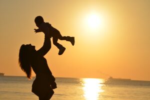 Mujer levantando a un niño en brazos durante el atardecer en un playa